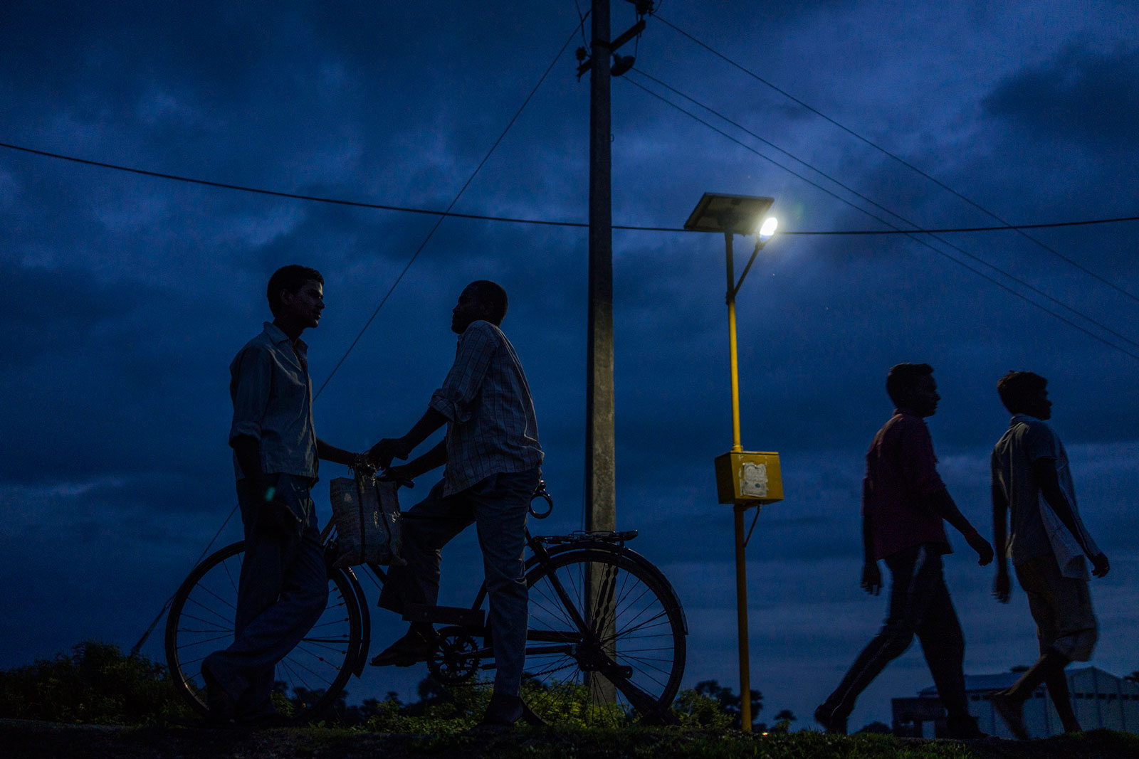 People walk past a light powered by energy from a solar-power microgrid at night in the village of Dharnai in Jehanabad, Bihar, India