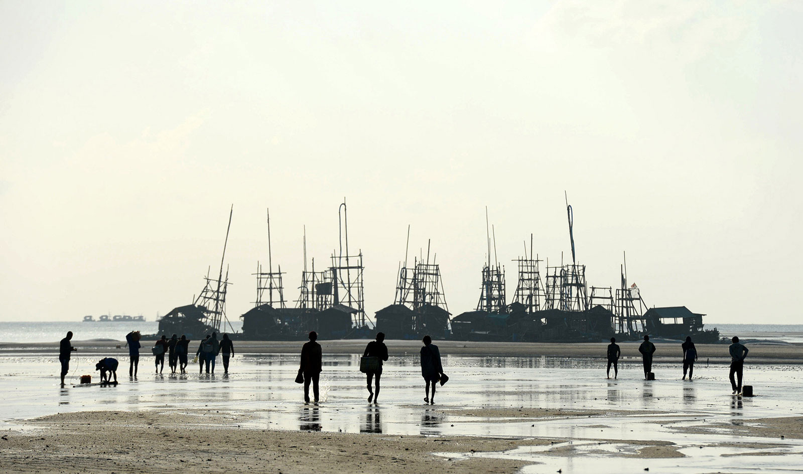 Workers walk toward wooden dredging rafts on the beach off the coast of Bangka Island, Indonesia