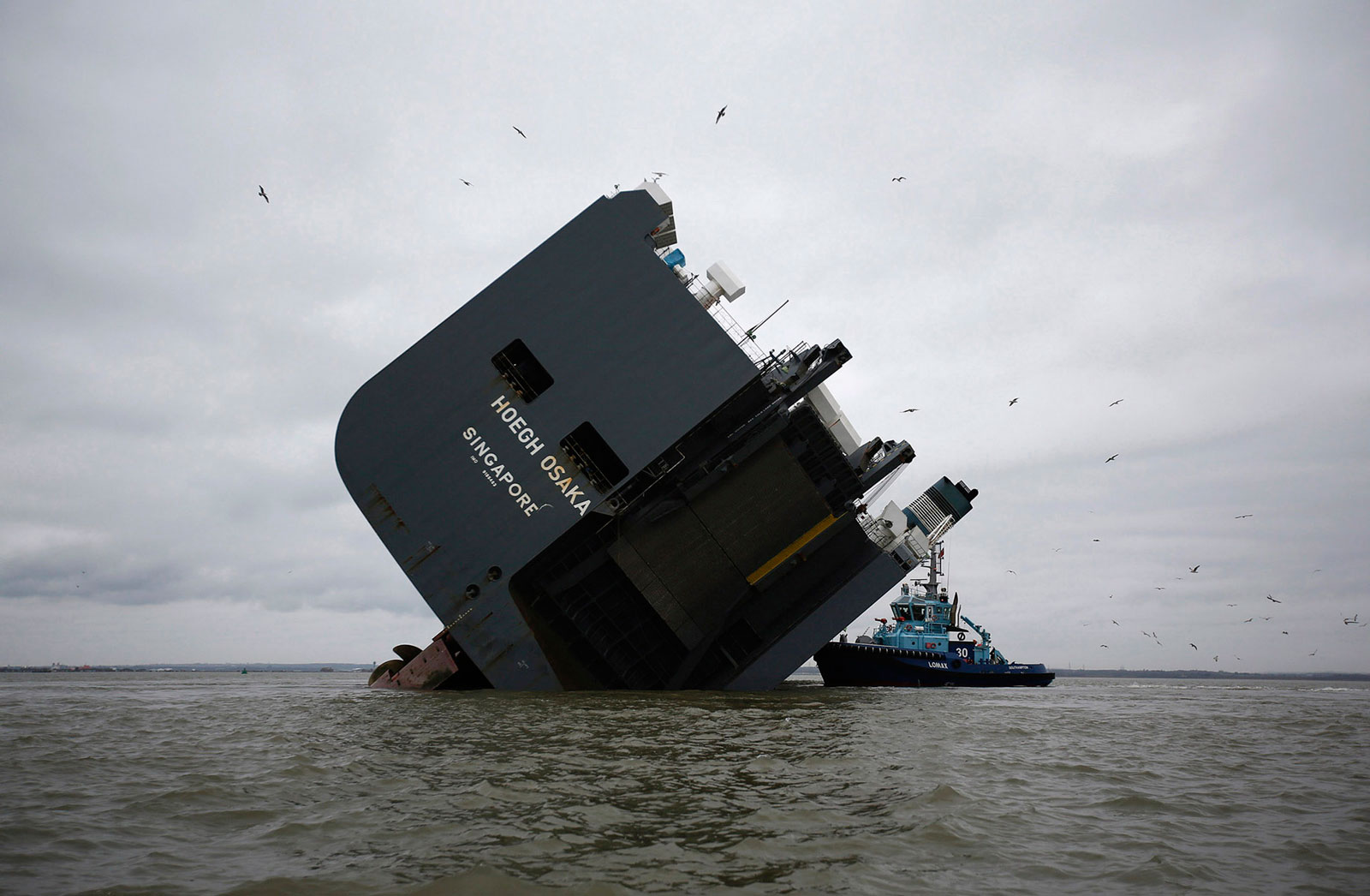 The Lomax firefighting tug, operated by Solent Towage, sits alongside the Hoegh Osaka ro-ro cargo ship, operated by Hoegh Autoliners, as it sits grounded on Bramble Bank in the Solent near Cowes, on the Isle of Wight, U.K.