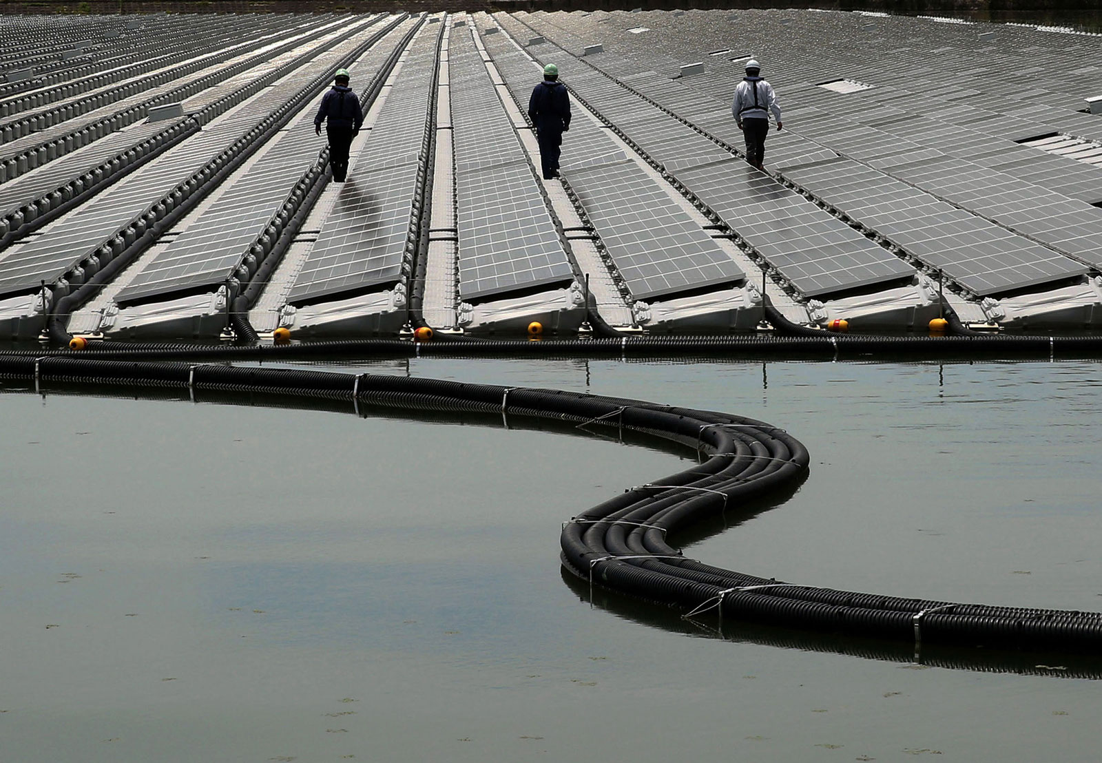 Workers walk between rows of solar panels at the 2.3-megawatt floating solar power station operated by Kyocera TCL Solar