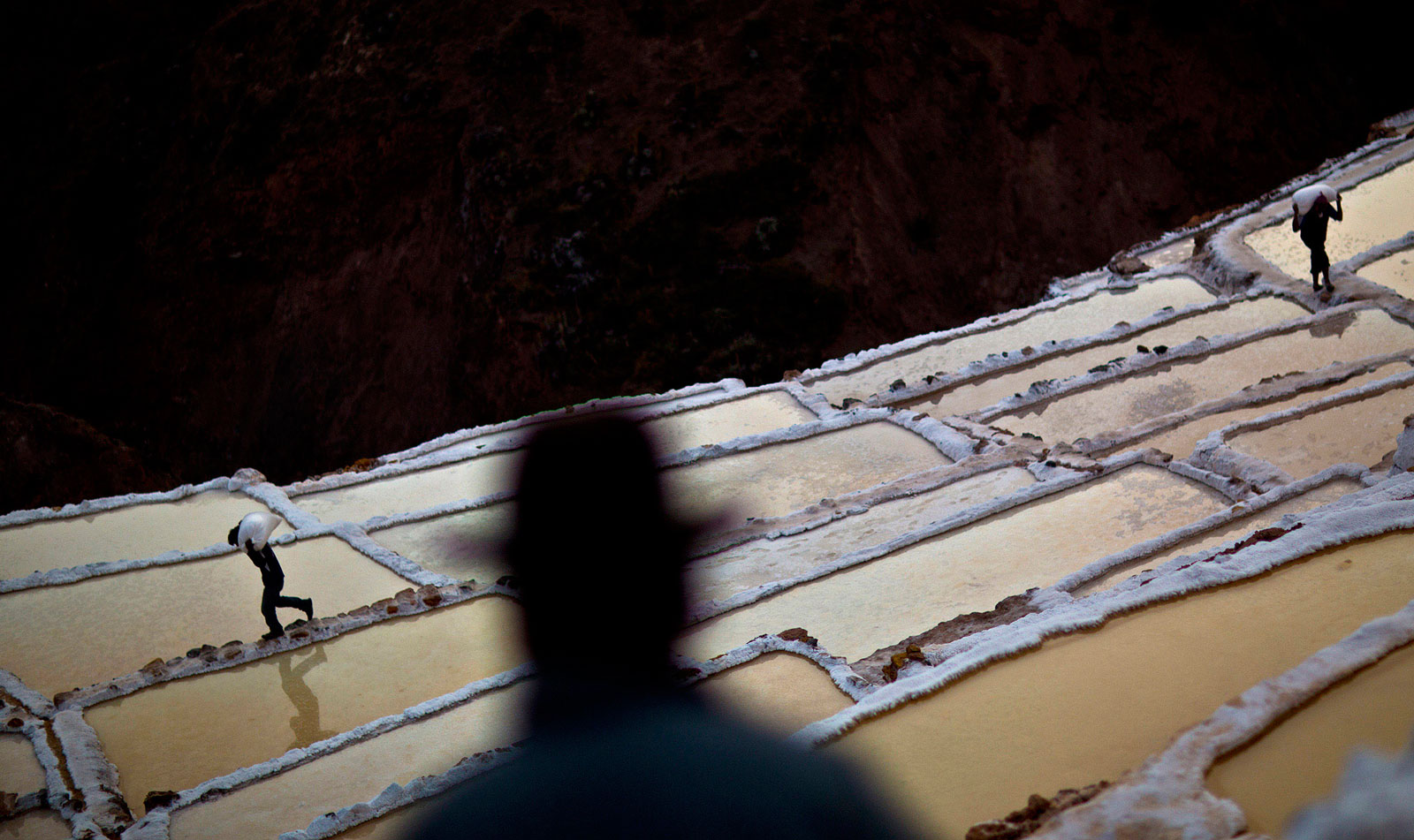 Miners carry bags of salt at the pre-Columbian salt mines in the Sacred Valley of the Incas in the Cuzco region of Maras, Peru